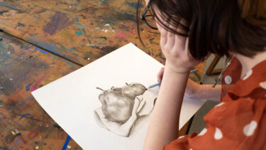 student works on a pencil drawing of a pear and apple