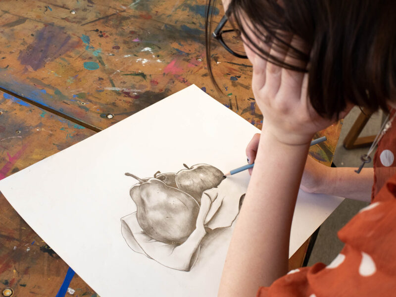 student works on a pencil drawing of a pear and apple