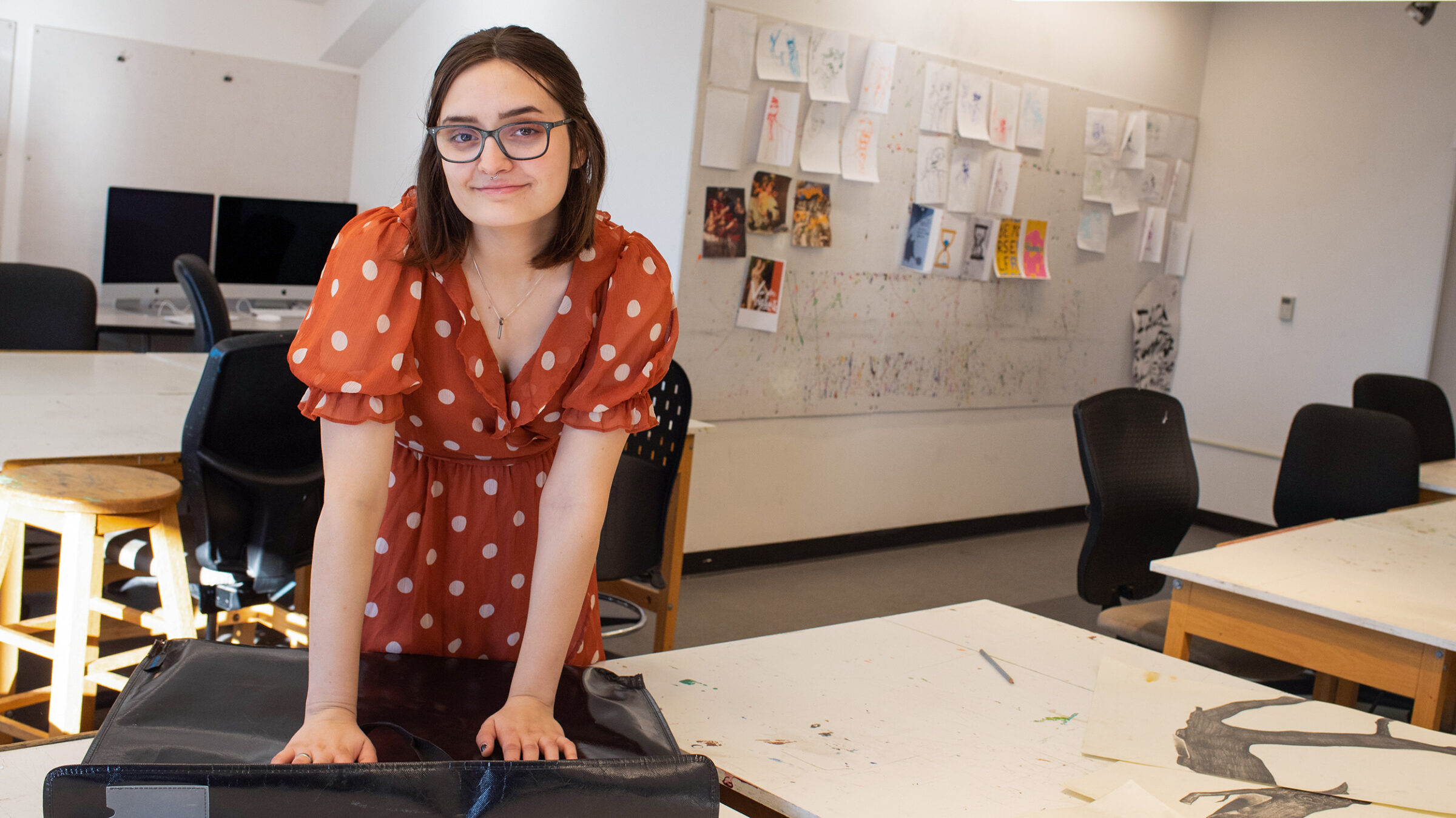 student stands over her art binder, looks at the camera