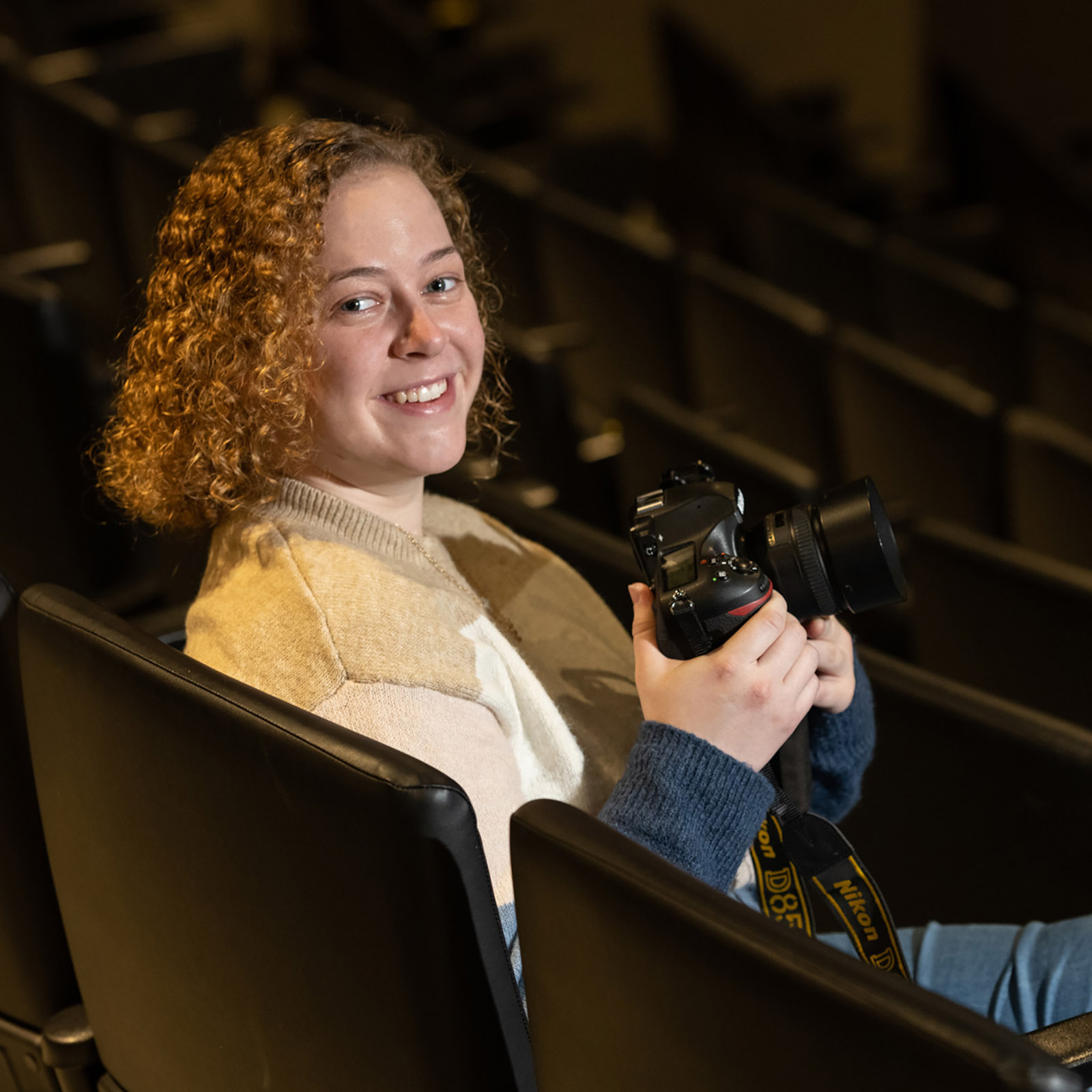 female sits in theater seat holding dslr camera