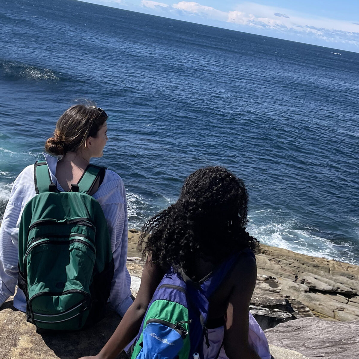 two students sit on a rocky beach looking out at the ocean