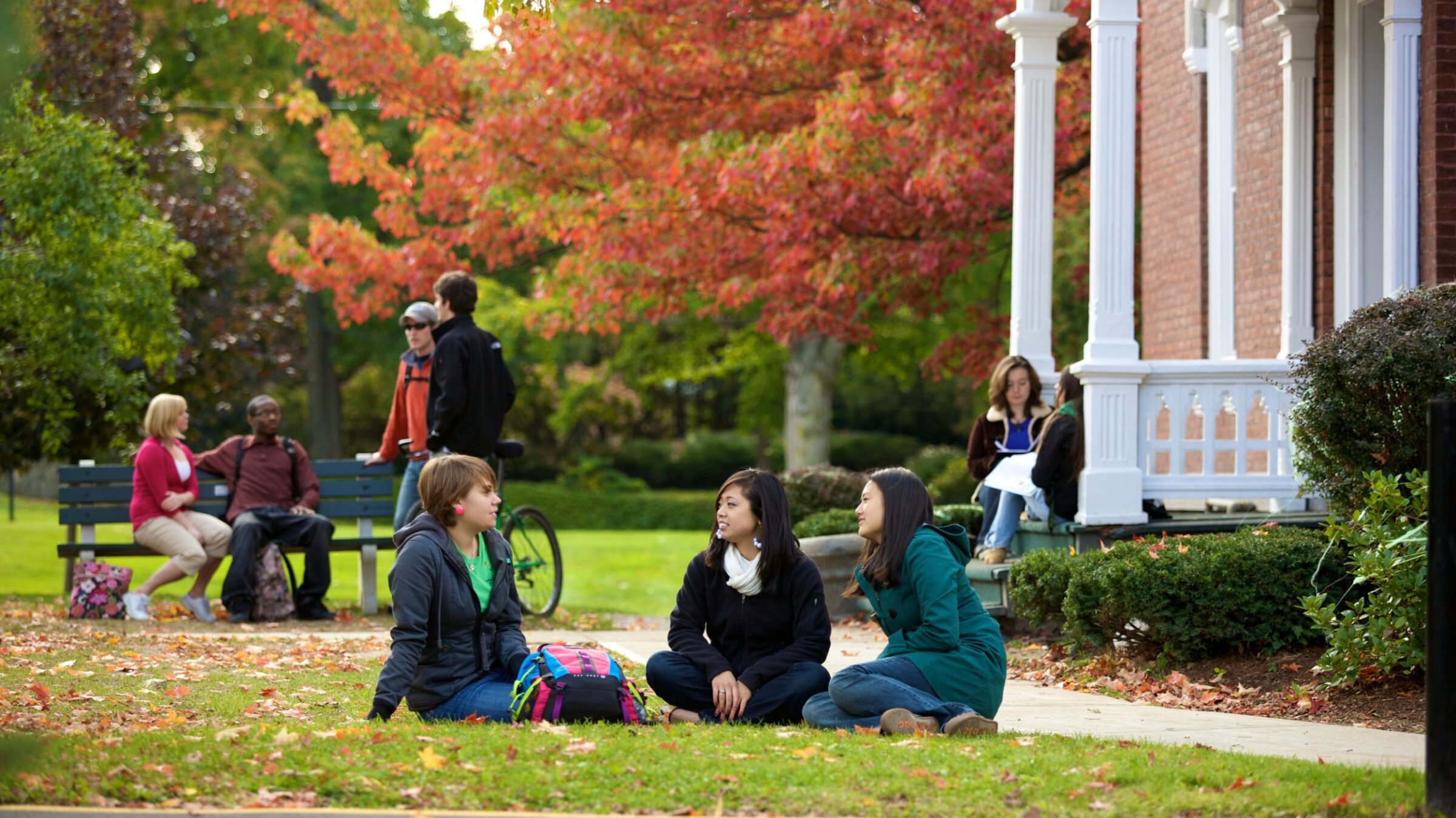 Students sitting outside a dorm hall in the grass during the fall season
