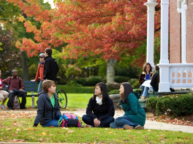 Students sitting outside a dorm hall in the grass during the fall season