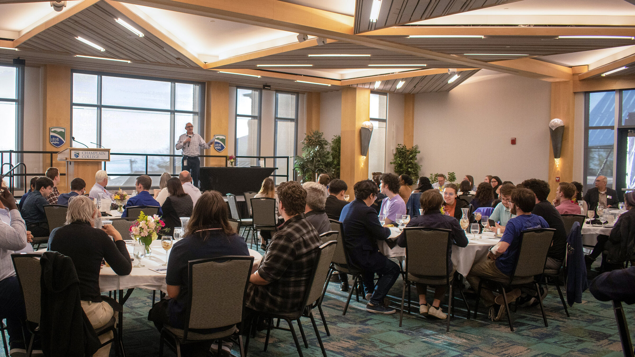 an event in the Champlain Room, people seated around tables, speaker at the head of the room