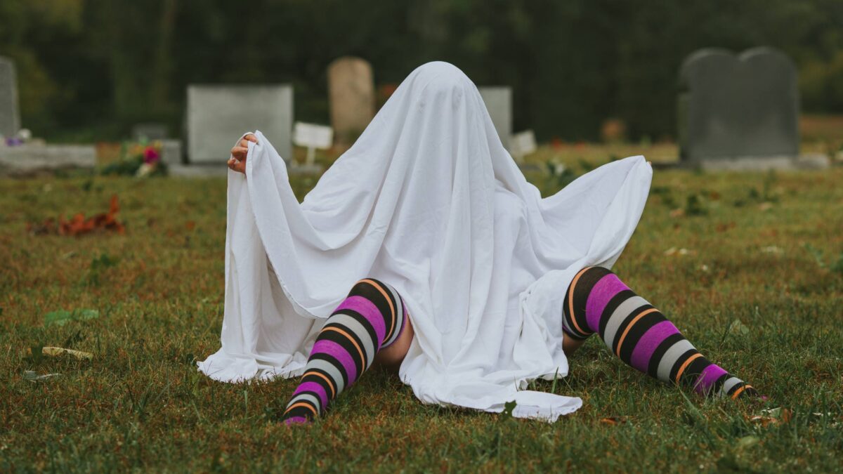 Person in a graveyard hiding under a sheet to look like a ghost