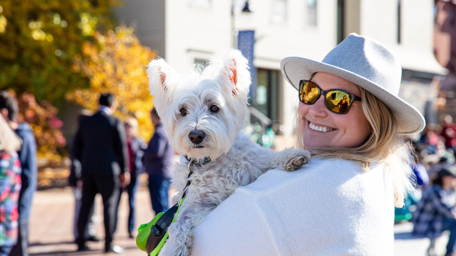woman in a hat and sunglasses holds her dog on her shoulder