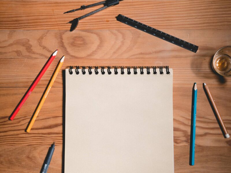 empty sketchbook on a table with various drawing utensils