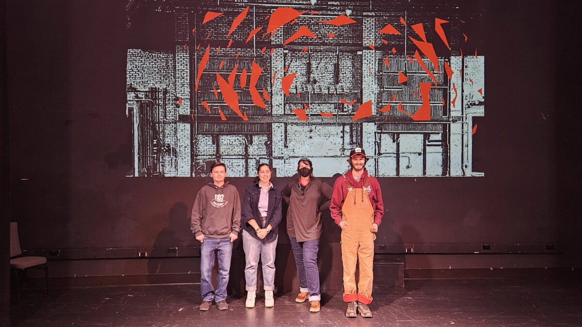 students stand in front of a large theater screen that is showing graphics