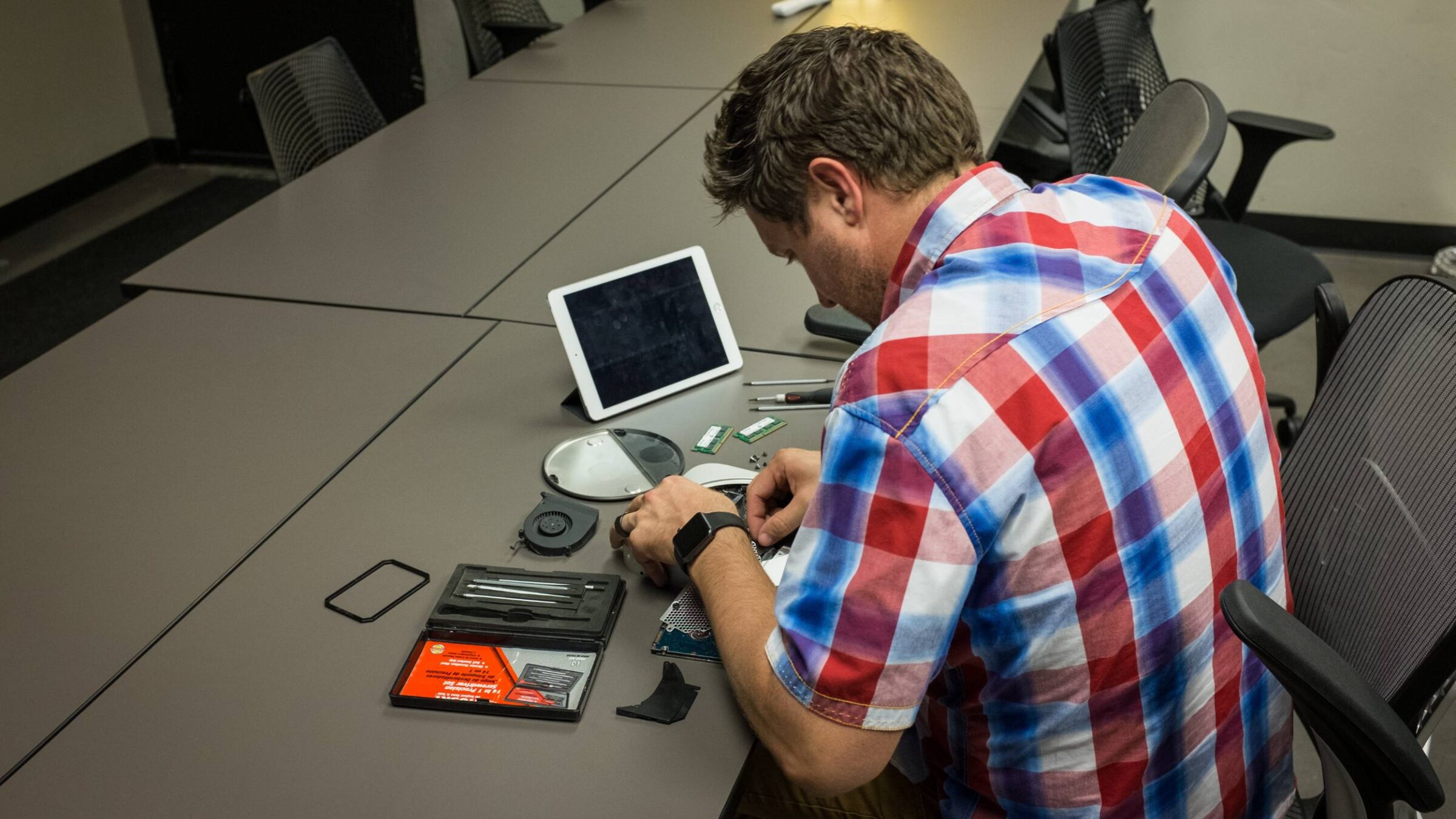 A staff member working on electronics at a table with an IPad