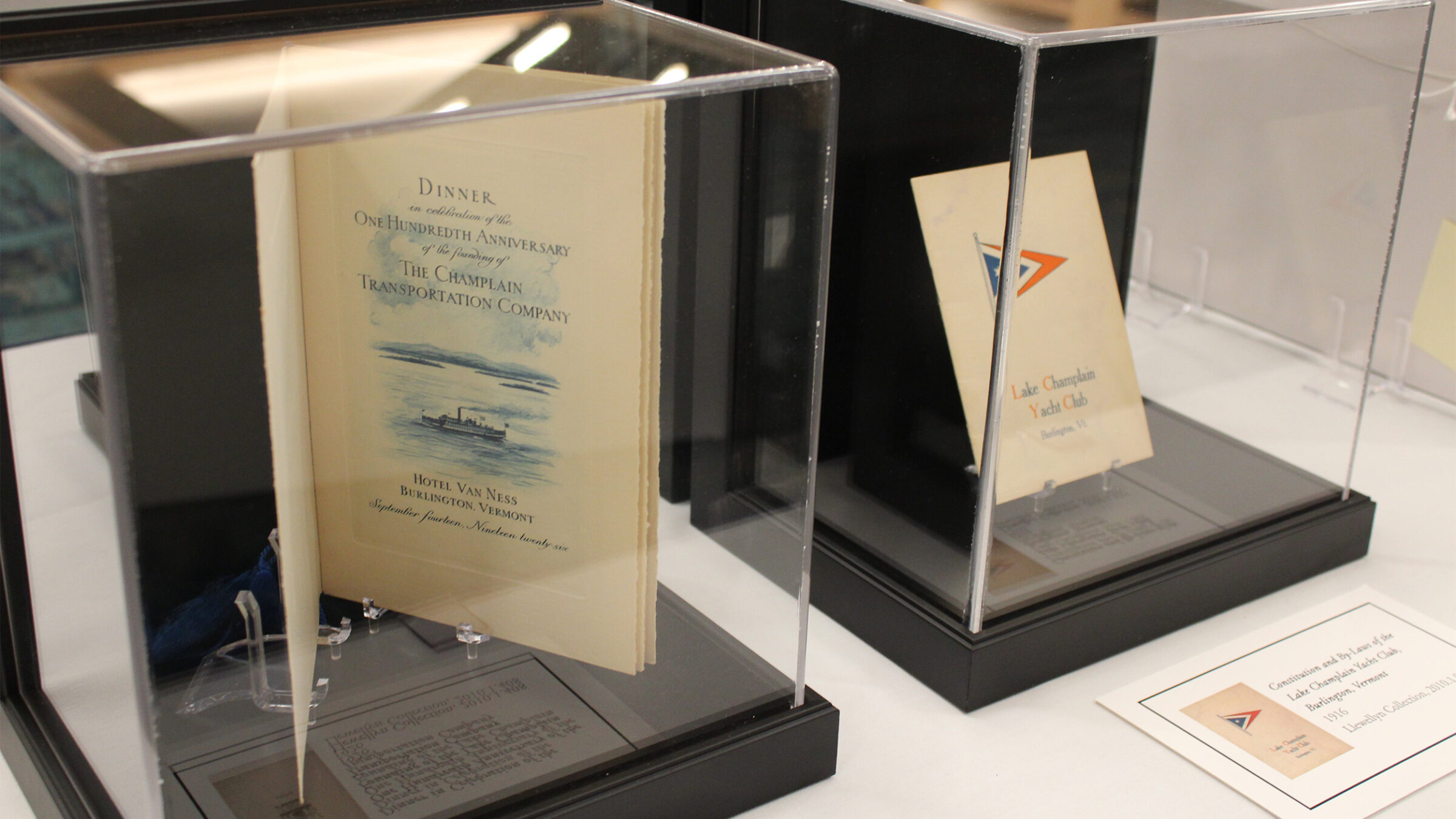 Menu for the 100th anniversary of the Champlain Transportation Company and pamphlet for the Lake Champlain Yacht club on stands under display glass.