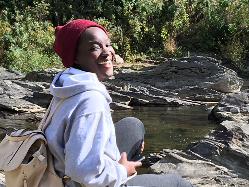 International student sitting outside by a river and smiling