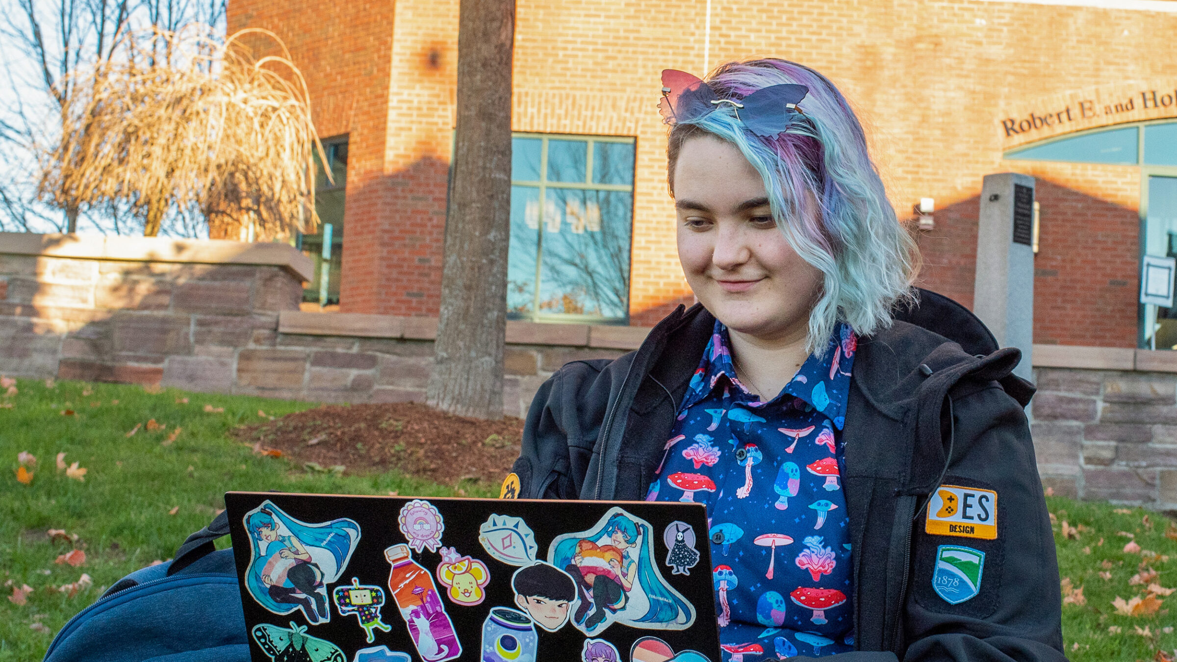 student uses a laptop while sitting on the lawn of the library