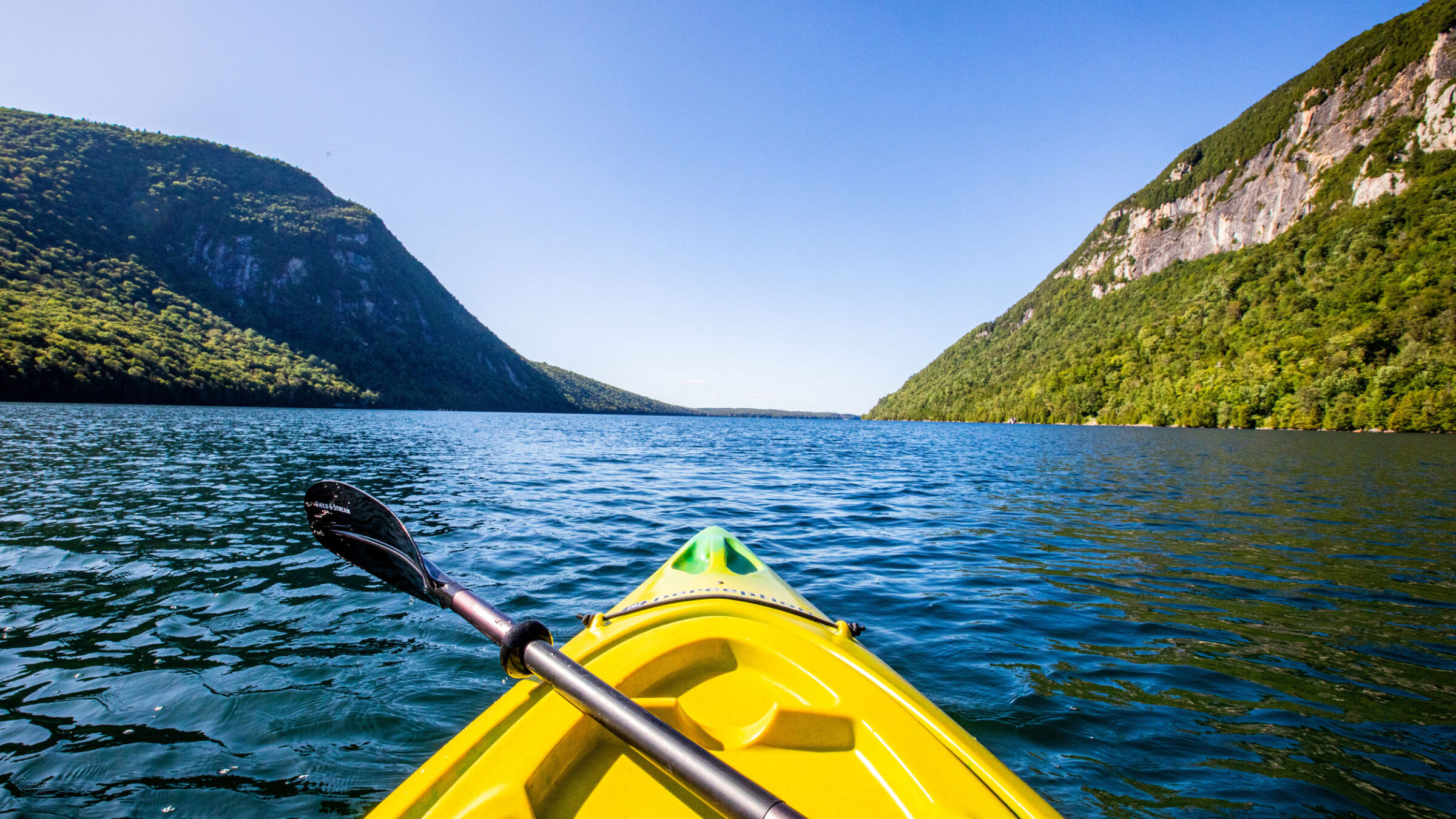 The tip of a kayak points toward mountains while resting in the center of Lake Willoughby.