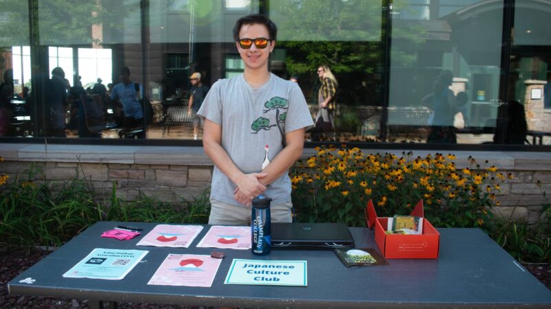 Student standing in front of IDX windows tabling a Japanese Culture Club wearing sunglasses