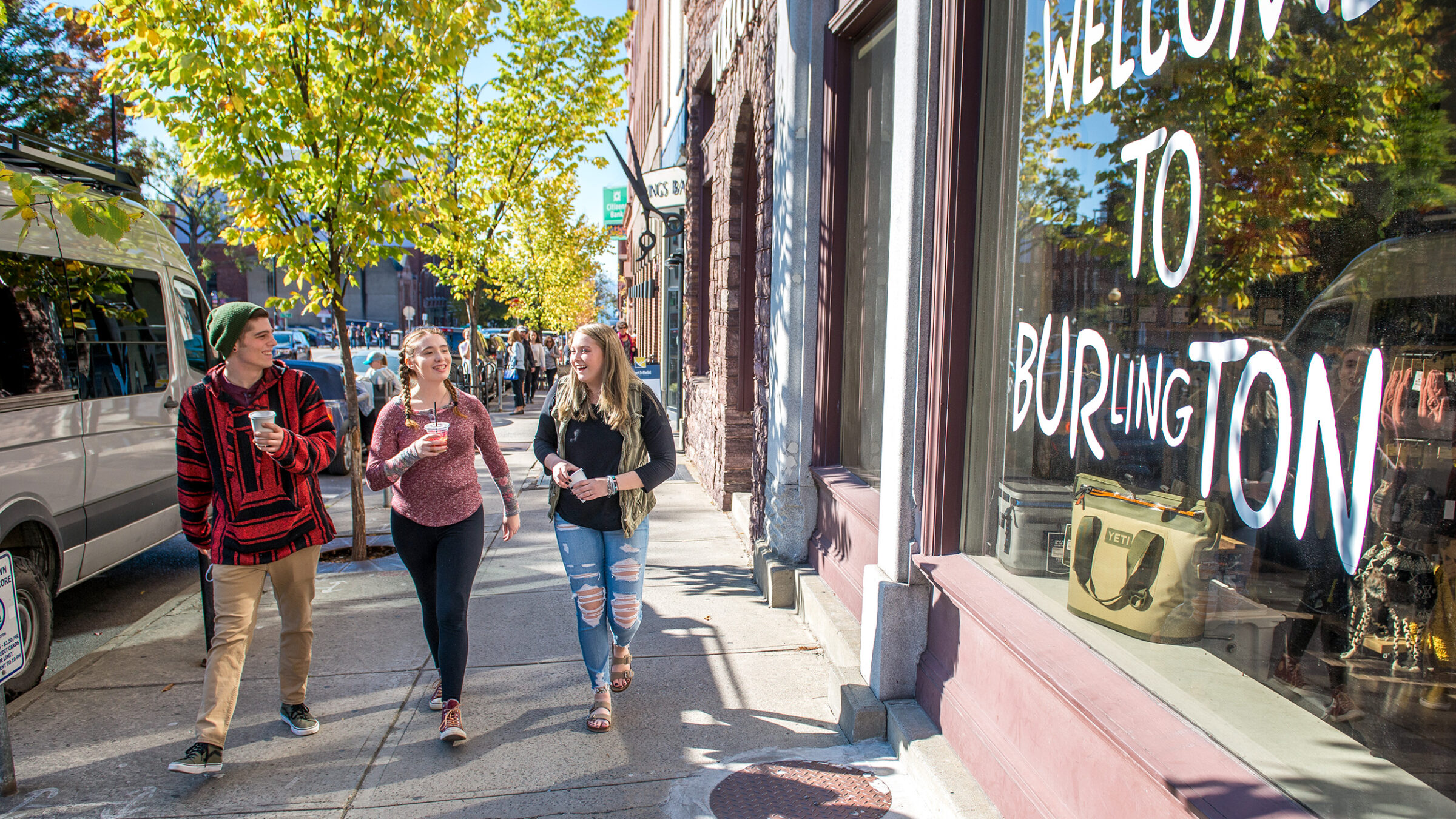 group of students walk along the street in Brulington, Welcome to Burlington painted in a business window