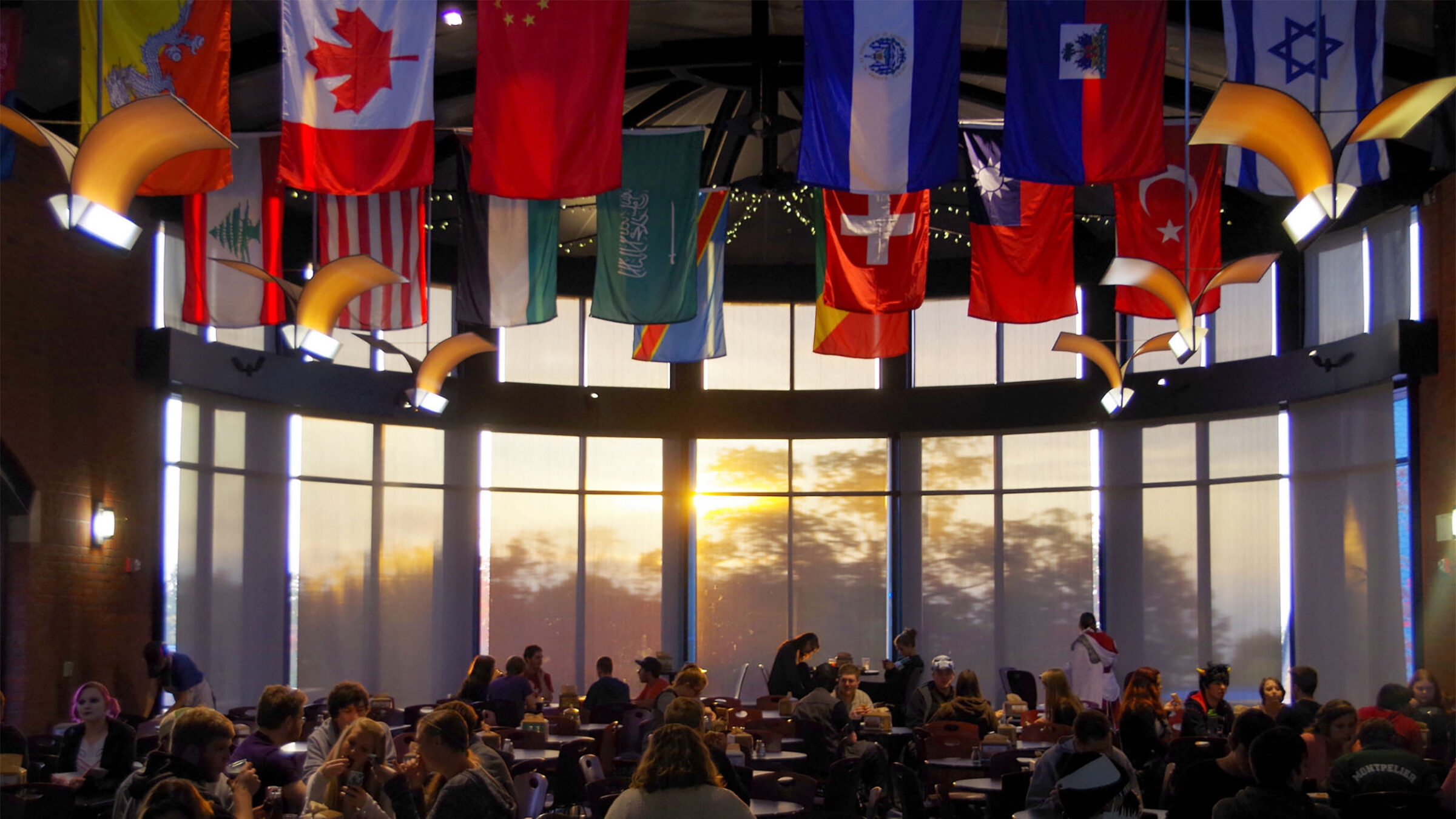 multicultural flags hang above the lively dining hall during sunset