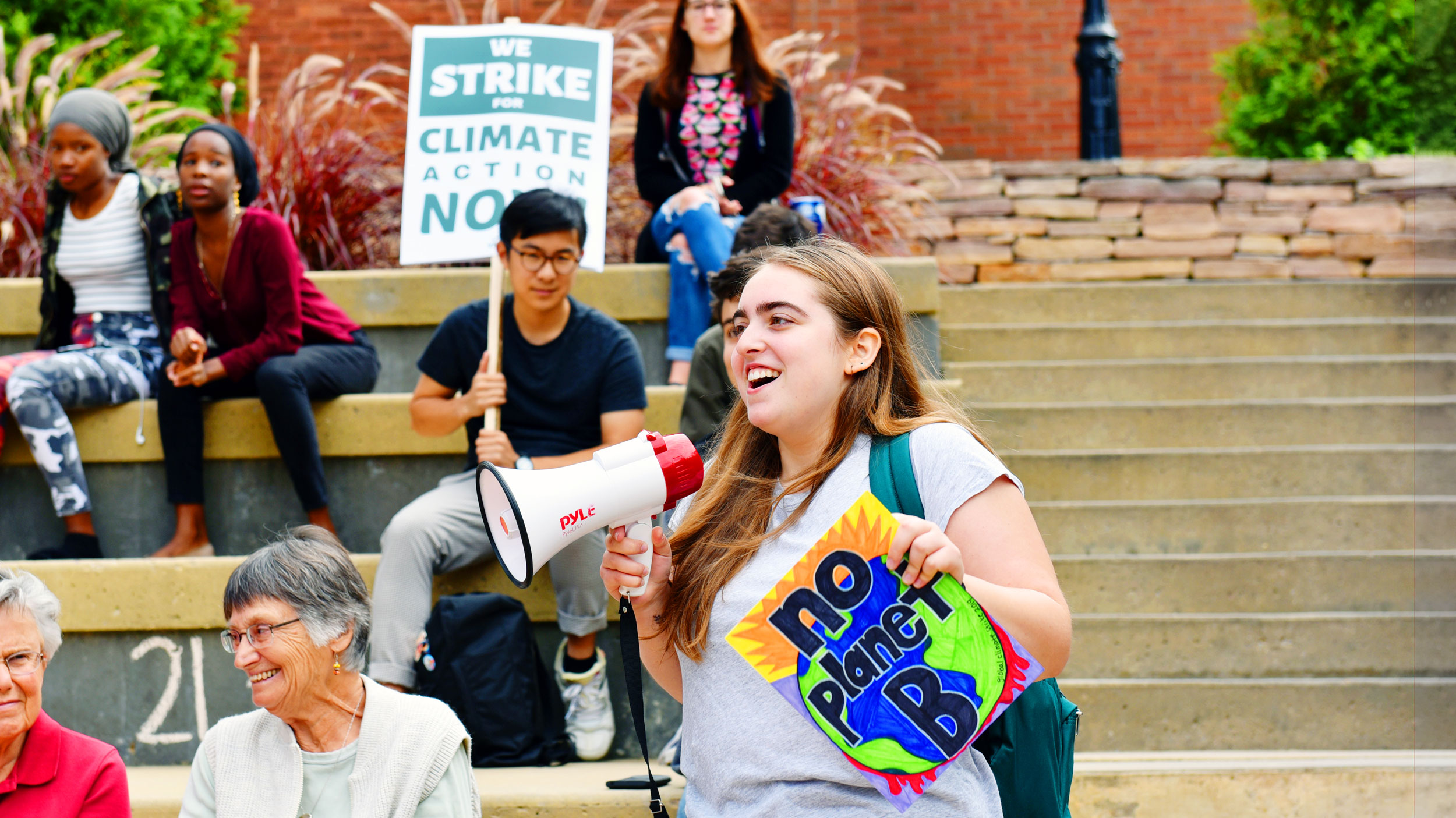 A student speaks into a megaphone at a climate rally and holds a sign that reads "No Planet B"