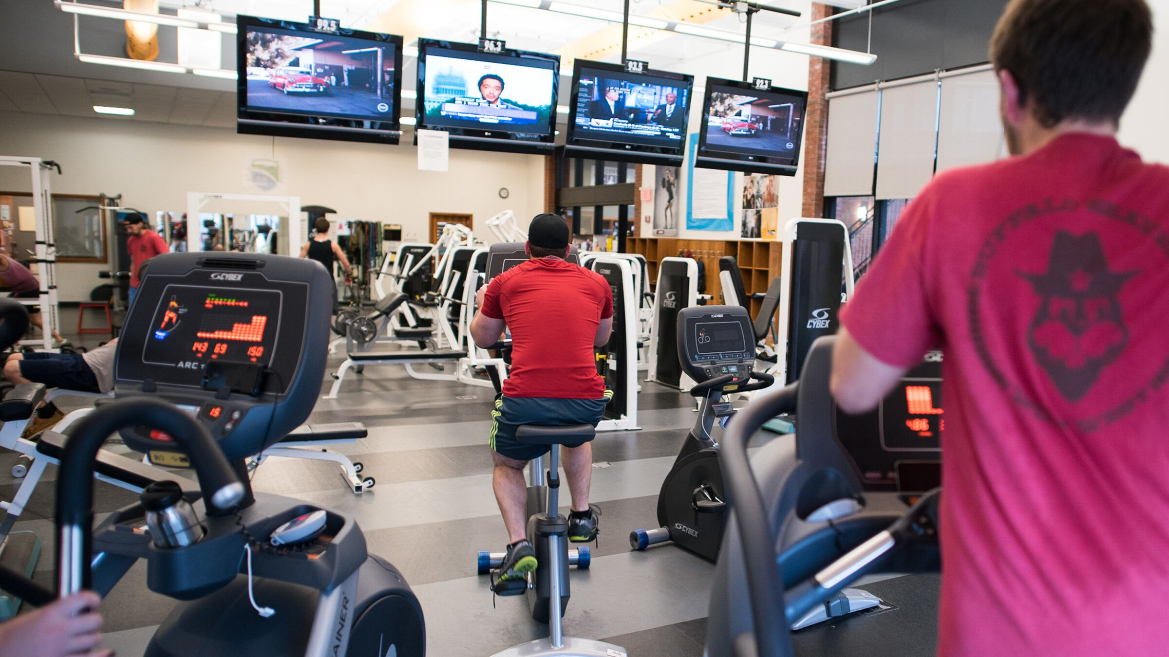 students use equipment while watching tv in the fitness center