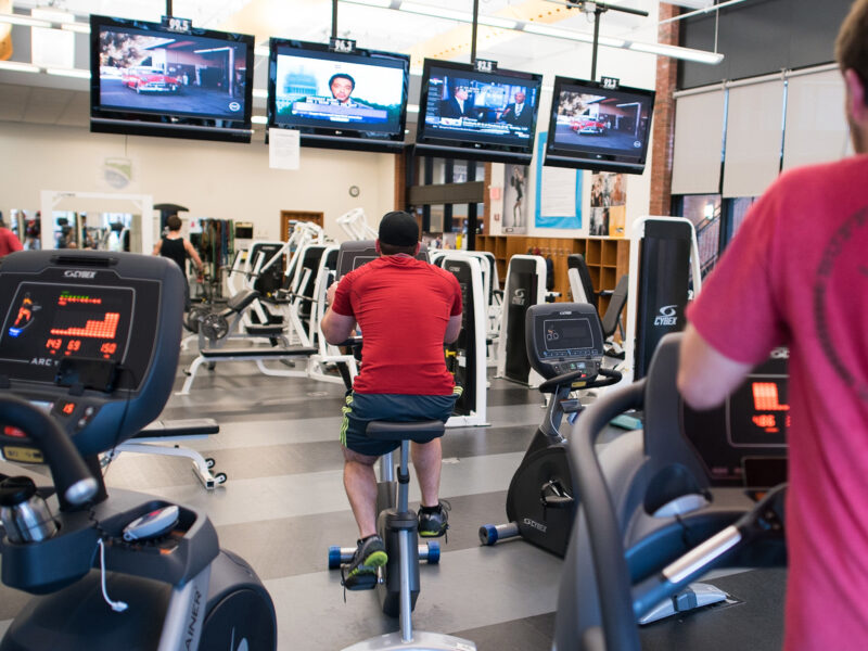 students use equipment while watching tv in the fitness center