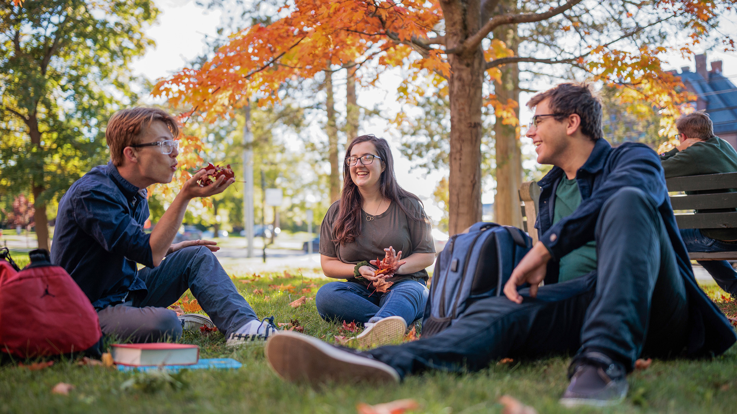 group of students site on the lawn during fall play with leaves