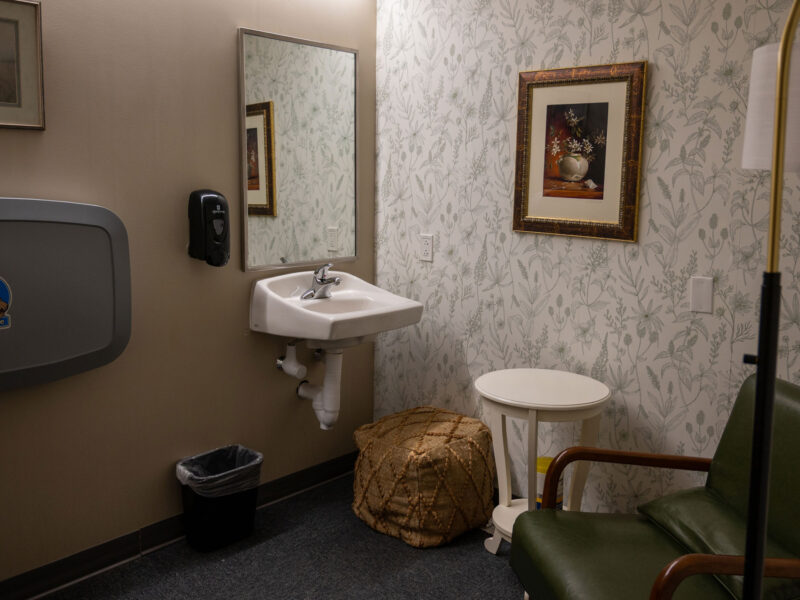 room with cute floral wallpaper and a sink, chair, table, and baby changing table