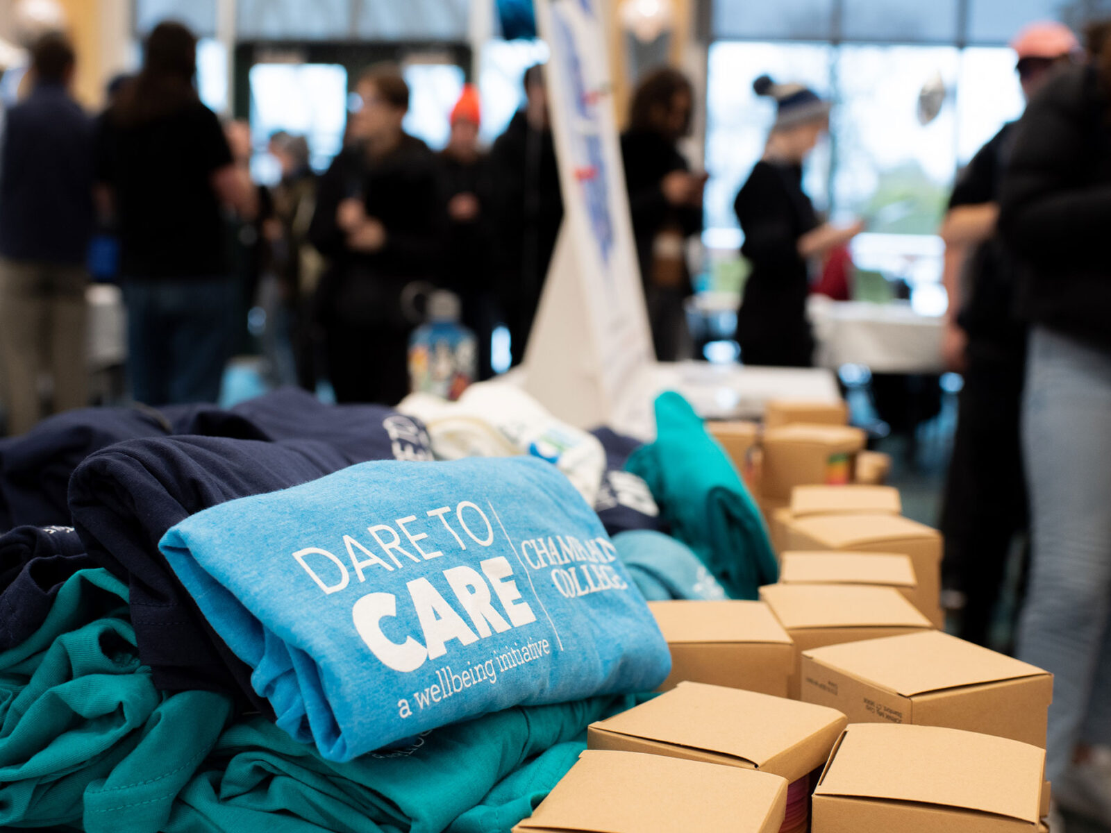 a blue tshirt that reads "dare to care a wellbeing initiative" sits atop boxes and a pile of tshirts
