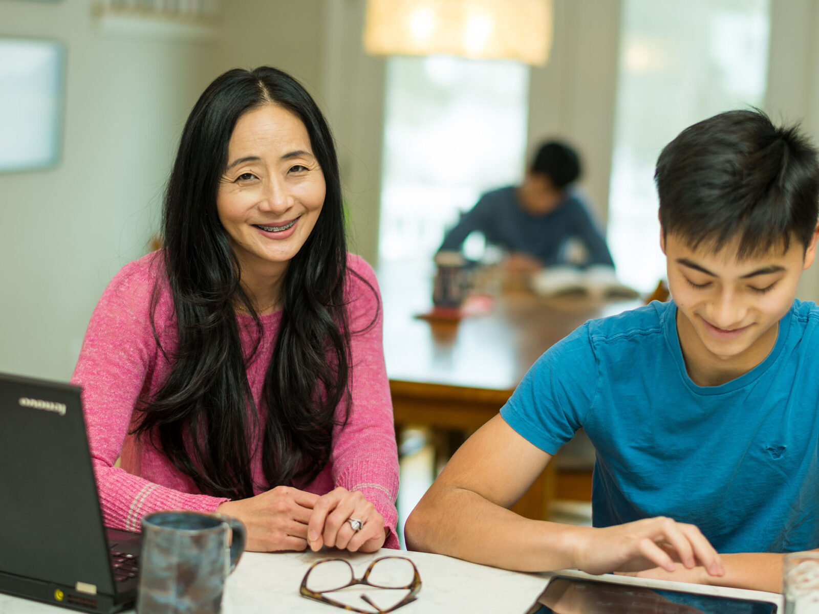 champlain college online student smiling for a photo while their child sits beside, looking at thier tablet.