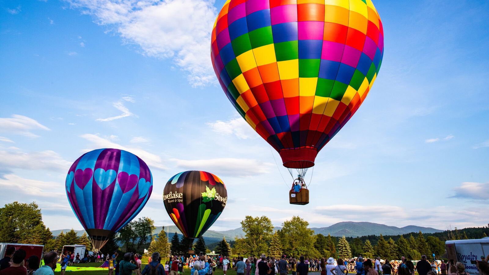 A trio of hot air balloons take off into a clear sky at a festival.
