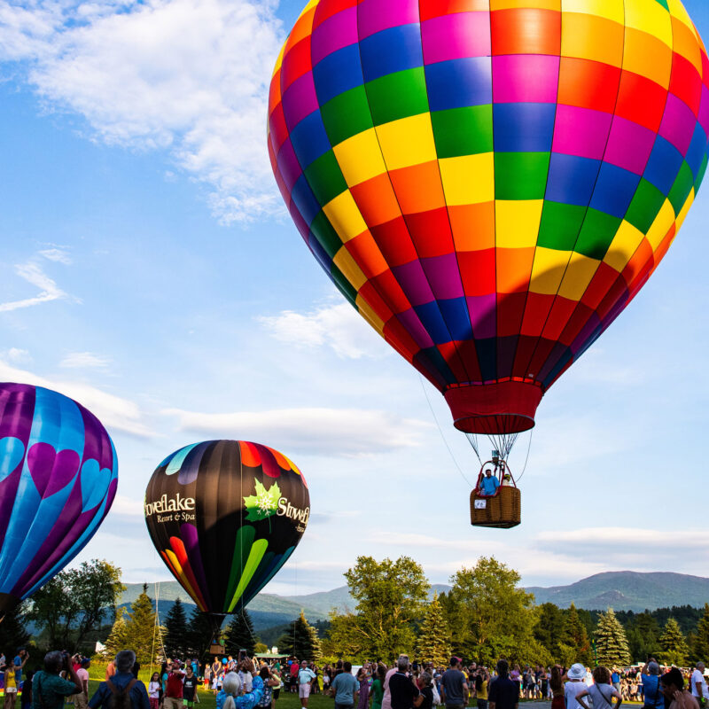 A trio of hot air balloons take off into a clear sky at a festival.