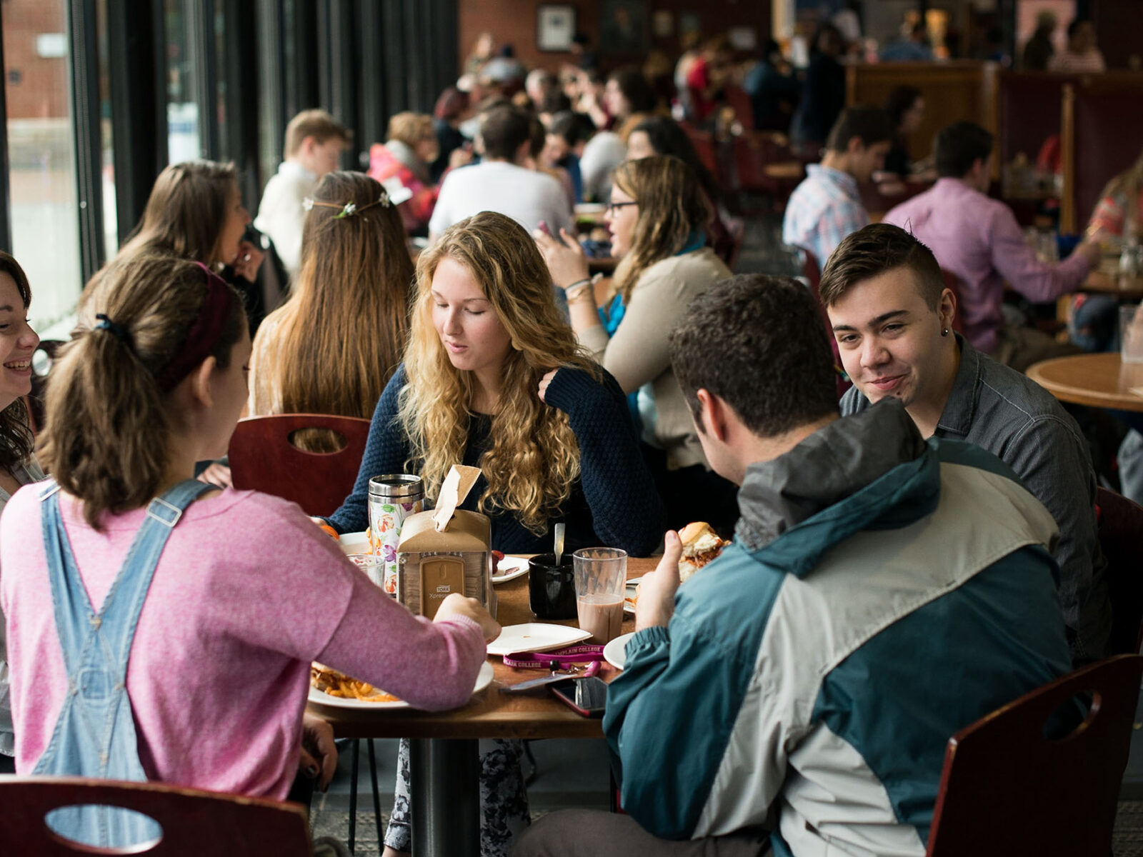 a group of students sitting around a table in the dining hall eating and talking