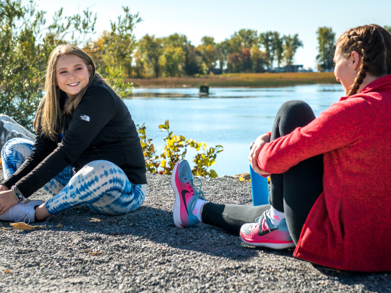 two students stretch before walking along the lake
