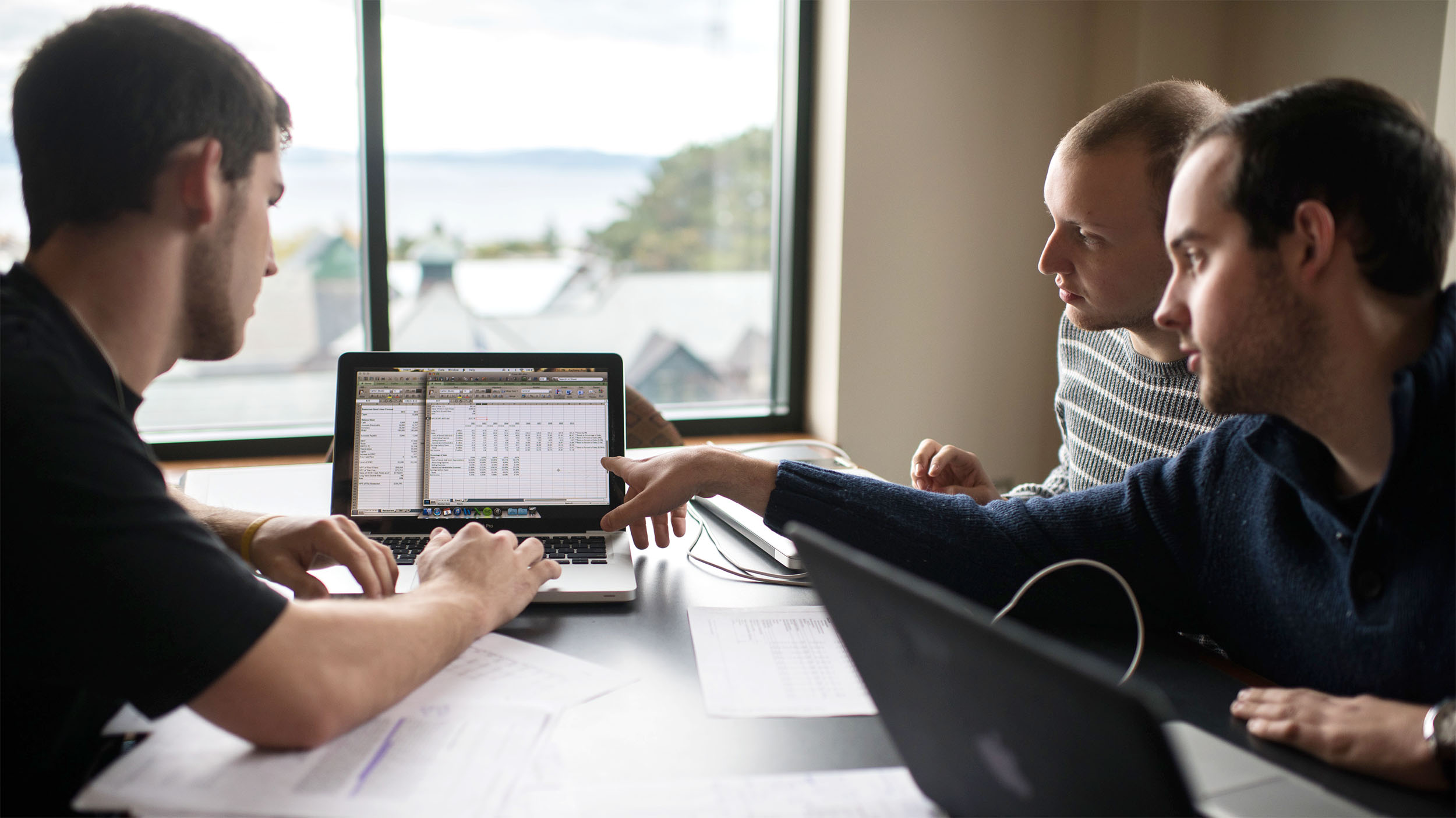Three students collaborate over a spreadsheet on a laptop
