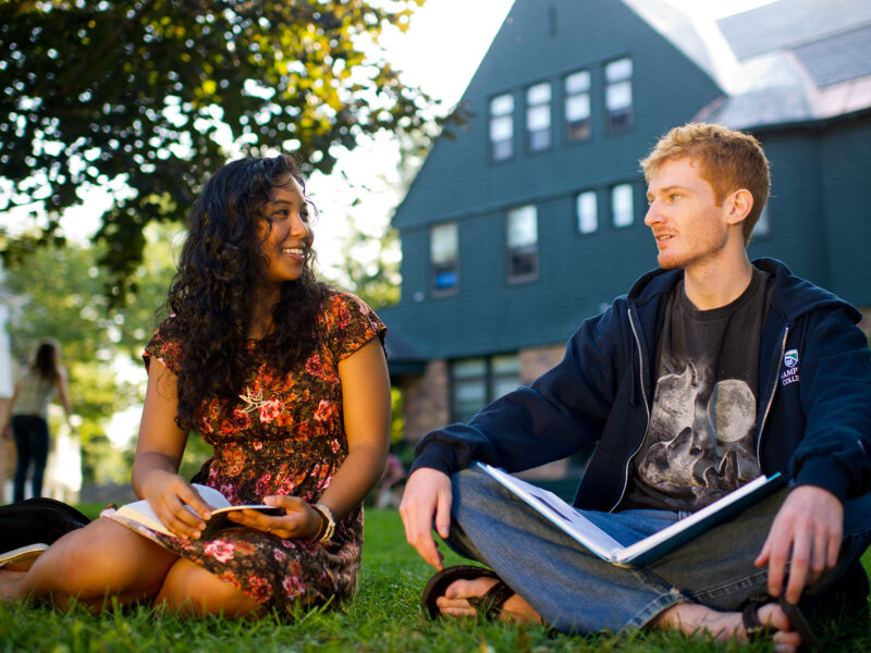 two students studying together in the grass on campus