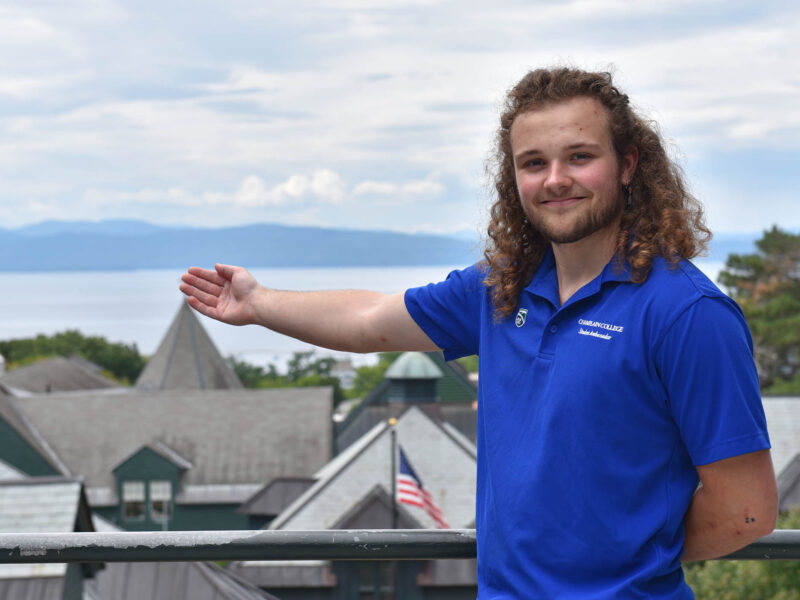 Student ambassador pointing toward beautiful lake view from Champlain College campus in Burlington, Vermont