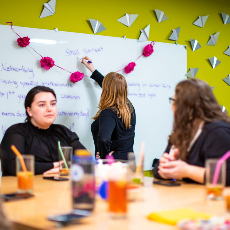 female students meet in the sarah ramsey lab, writing on a whiteboard