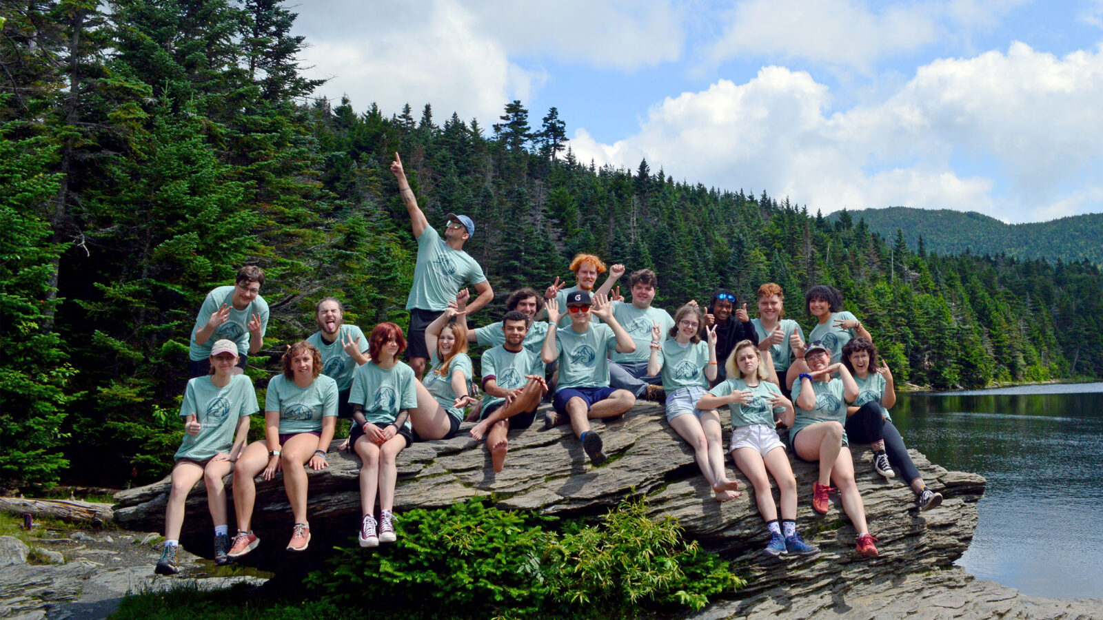 large group of students sitting on a rock at sterling pond with matching green Summer Launch 2023 shirts