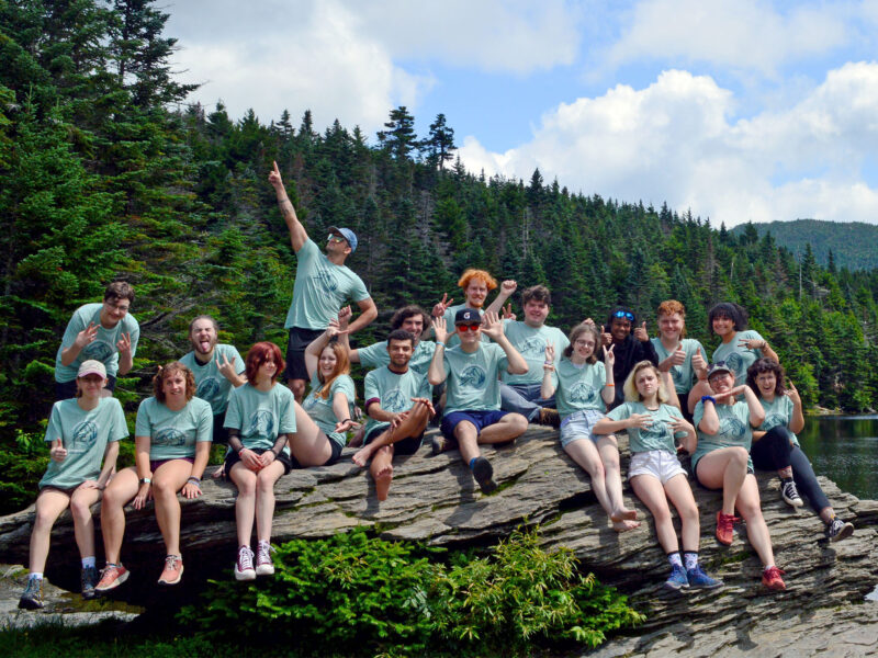 large group of students sitting on a rock at sterling pond with matching green Summer Launch 2023 shirts