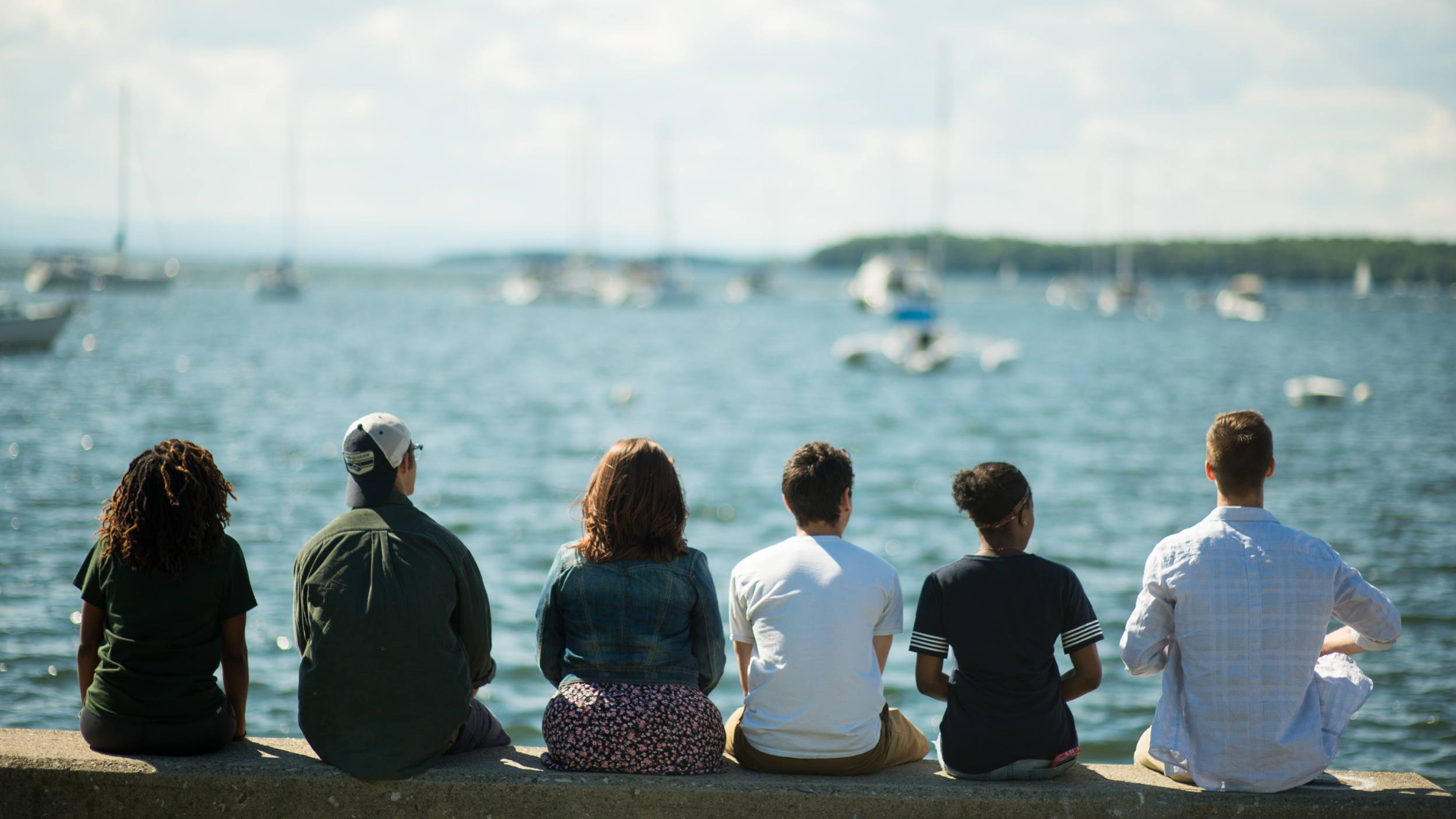 Students sitting near the lake with their backs toward the camera