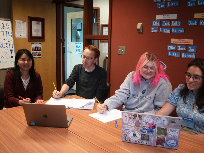 four students sit at laptops in a conference room while studying and receiving peer mentorship