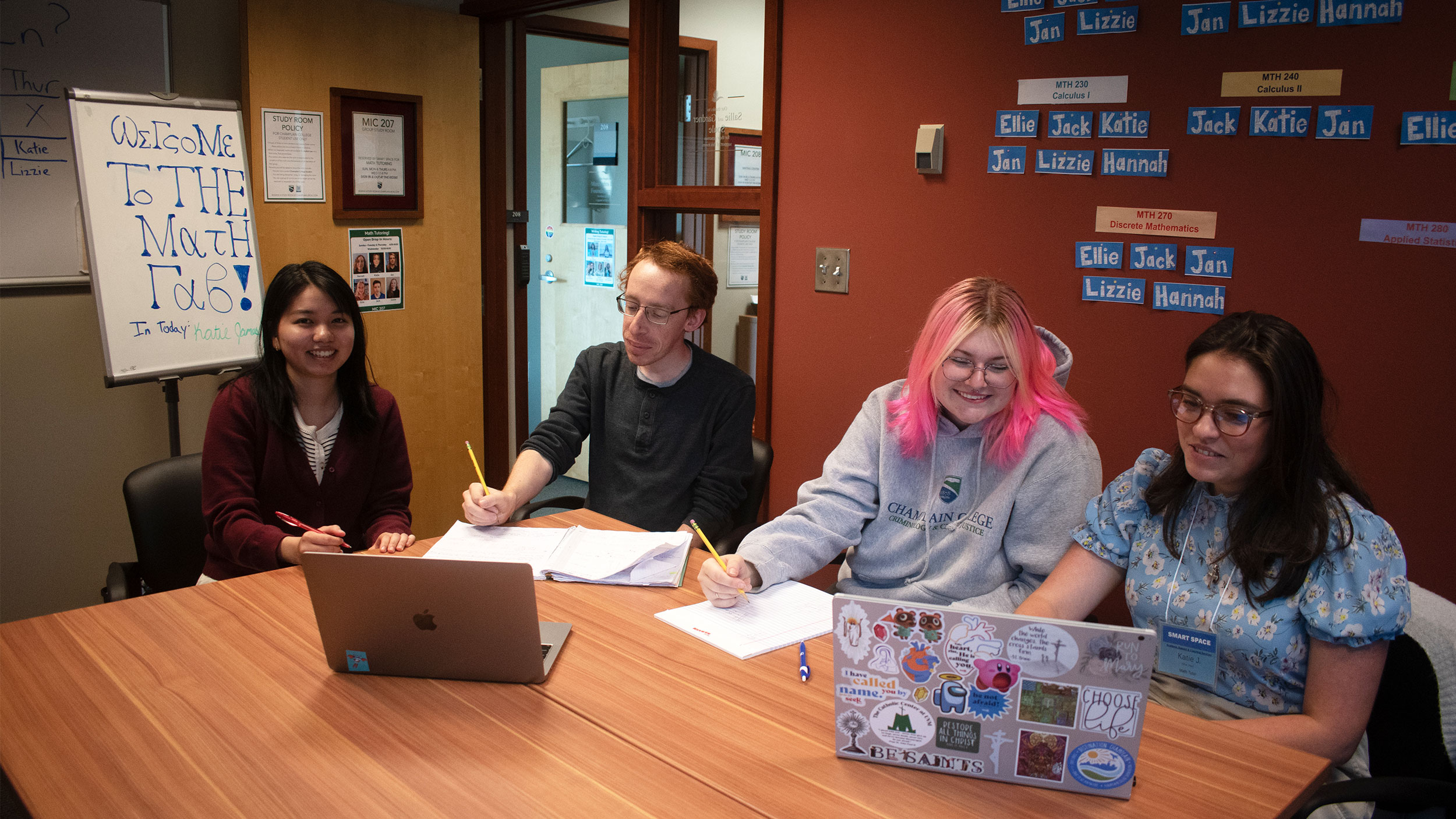 four students sit at laptops in a conference room while studying and receiving peer mentorship