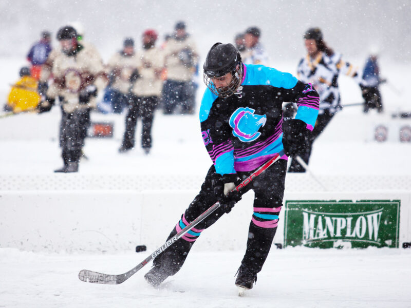 A hockey player takes a shot with the puck during a game played on a frozen lake.