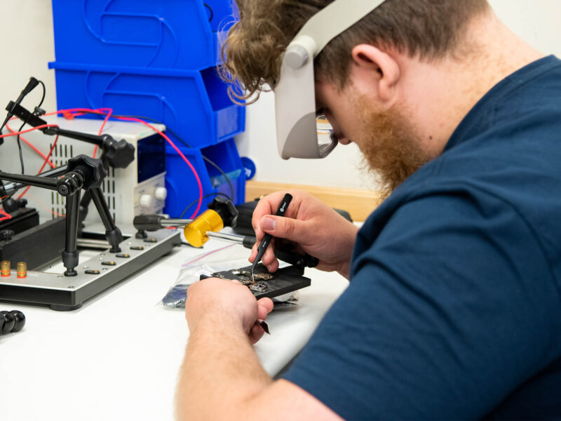 a cybersecurity student working on small computer components in a workshop