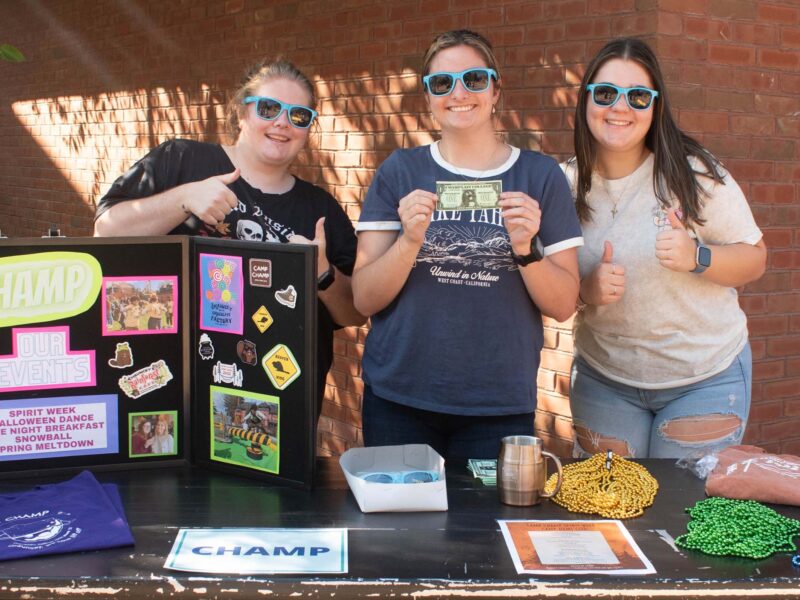CHAMP students with a poster describing their club holding chauncey bucks during the activity fair