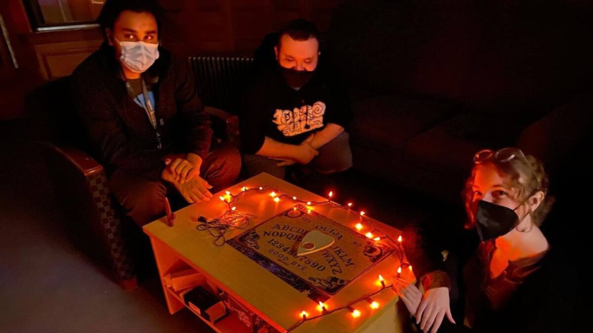 A group of three students in the supernatural club surrounding a Ouija board