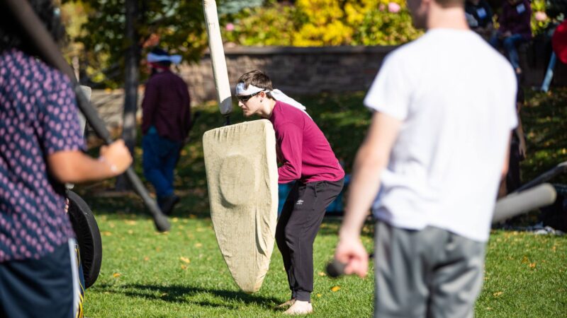 students participating in the hearthlight club on campus in the quad holding a foam sword and shield