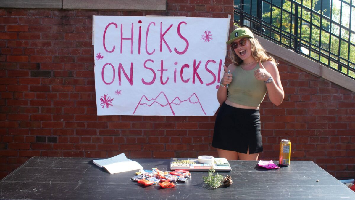 Student standing in front of the sign "Chicks on Sticks" at the club activity fair