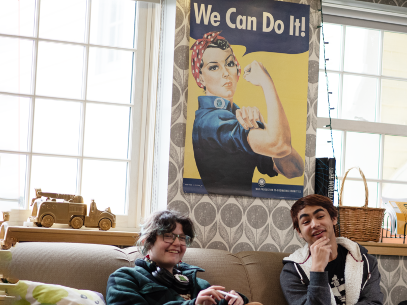 Two students hang out in the Women's and Gender Center, seated below a Rosie the Riveter sign.