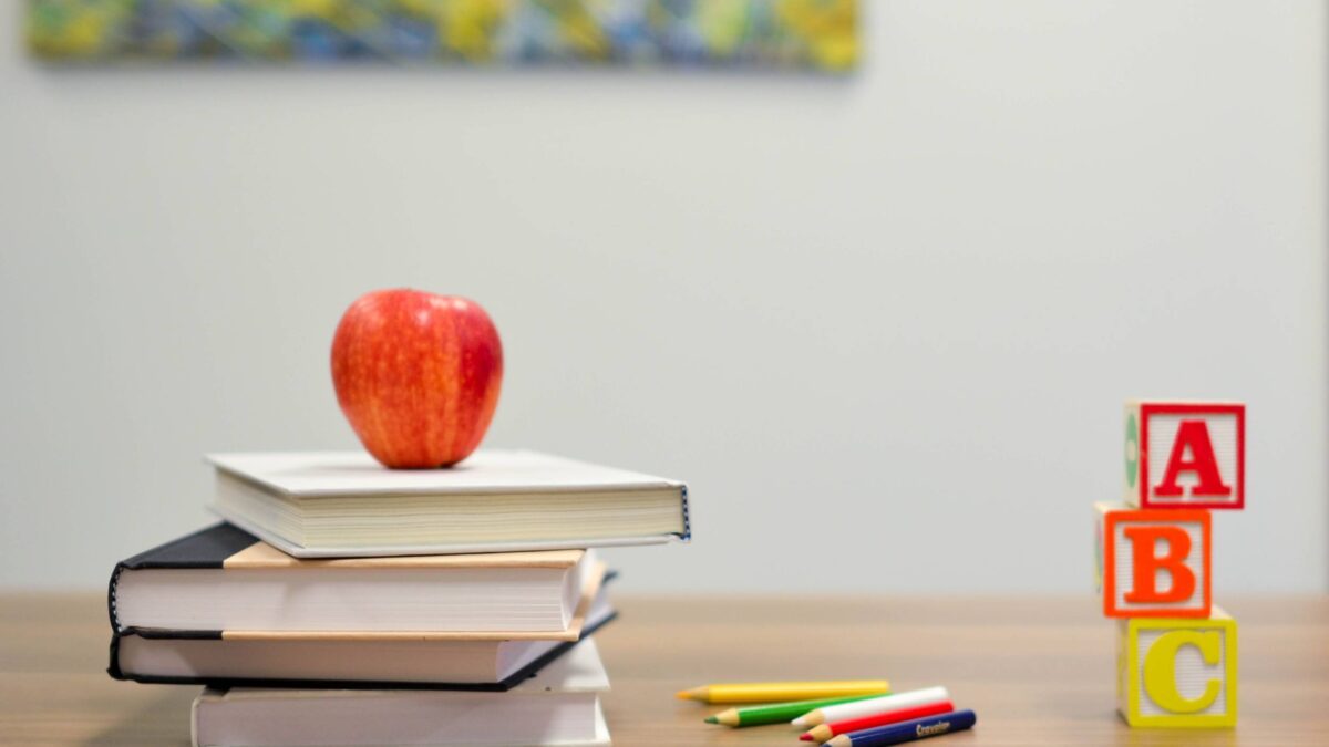 Apple on top of books, block letters A B and C stacked on a table next to colored pencils