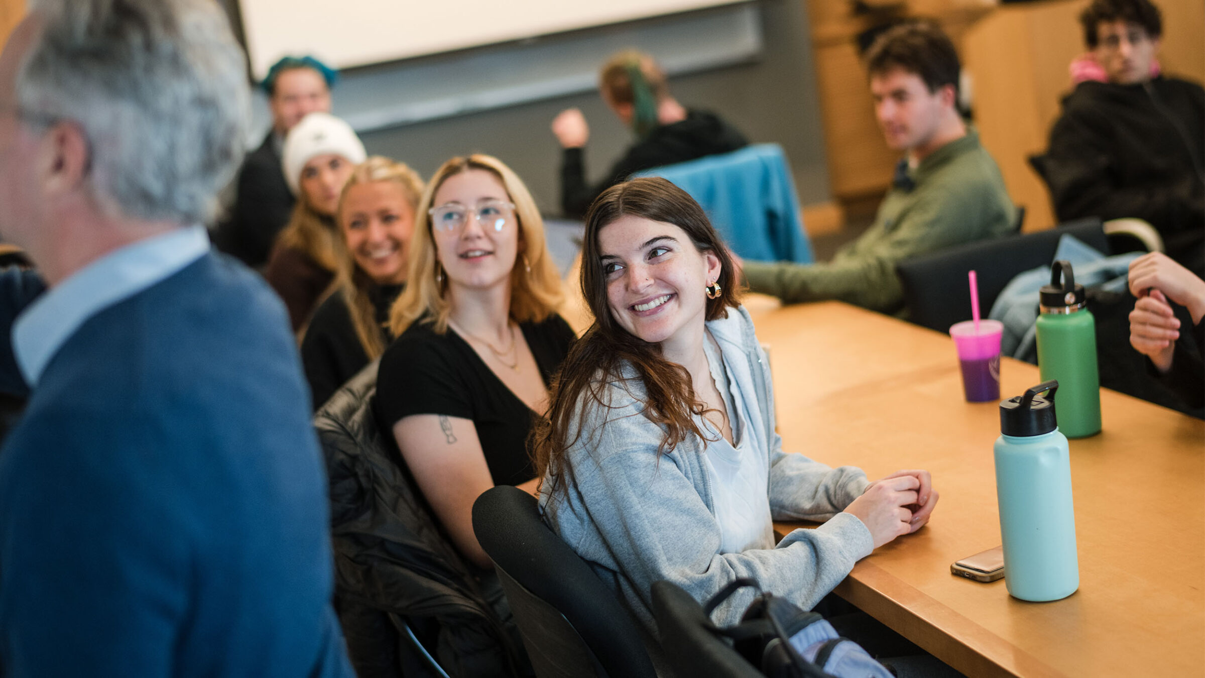 students at a table watch the professor write on a white board