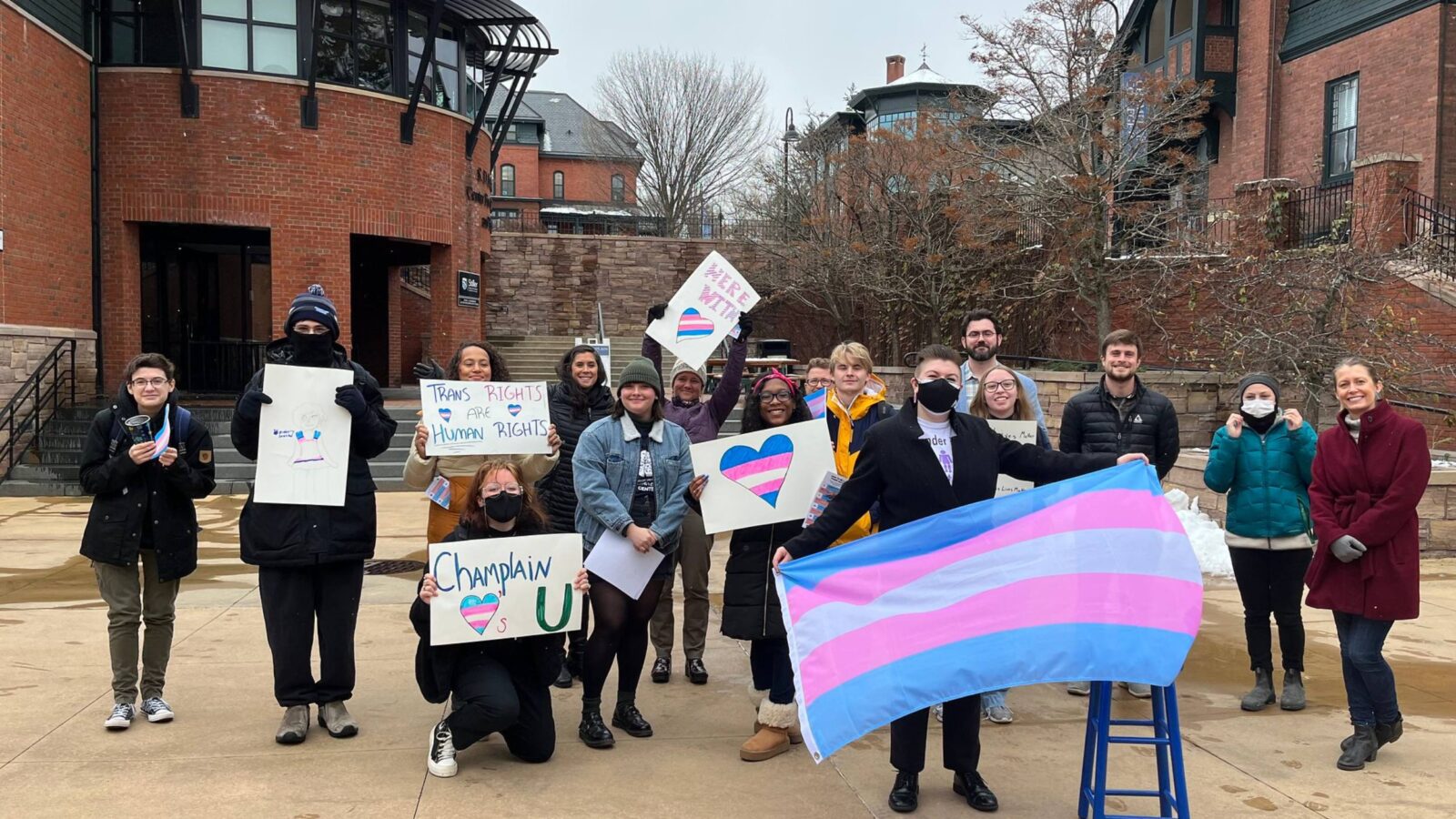 Snowy trans day of remembrance student group posing with signs and flags in the courtyard